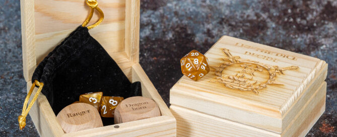 Two wooden boxes, one open with two large dice inside it and a selection of polyhedral dice. The other box is closed and is engraved with let the dice decide.