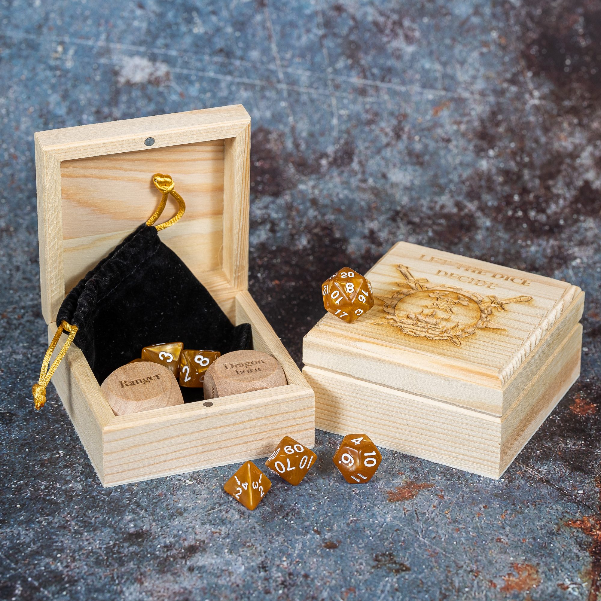 Two wooden boxes, one open with two large dice inside it and a selection of polyhedral dice. The other box is closed and is engraved with let the dice decide.
