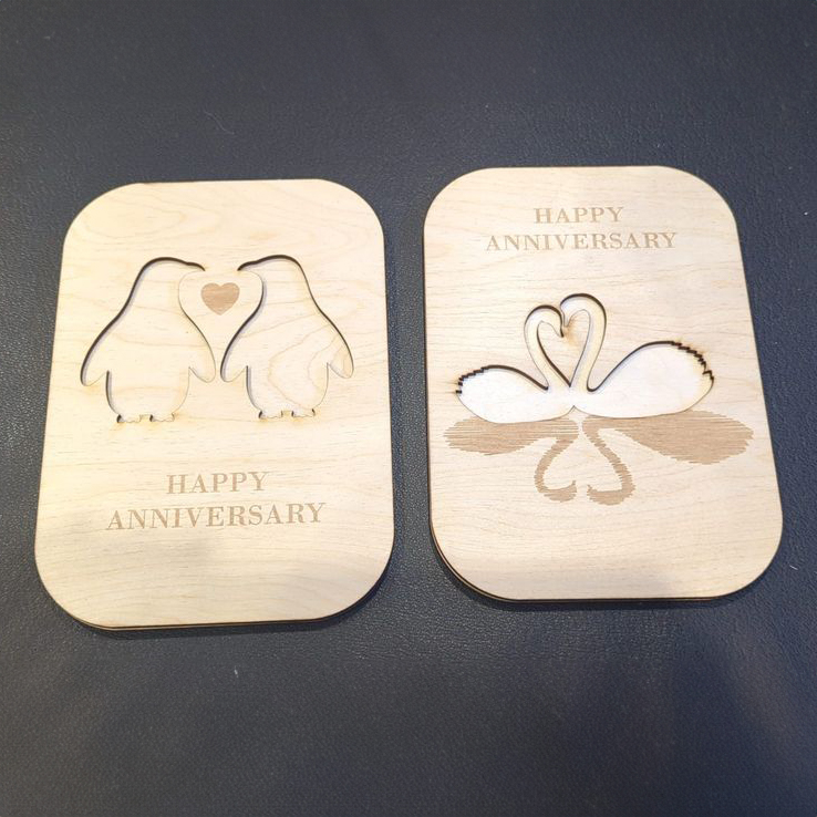 Laser cut out images of penguins and swans each forming hearts and the text Happy Anniversary underneath.