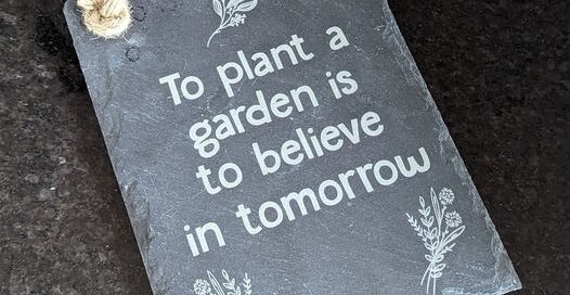 Slate sign laser engraved with To plant a garden is to believe in tomorrow and some floral imagery.