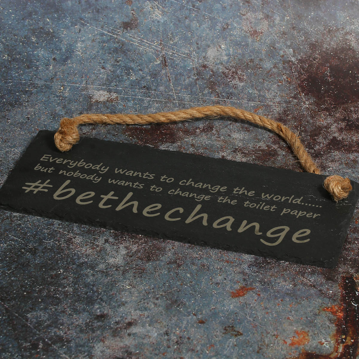 Engraved slate sign with a message about changing the toilet paper with jute rope.