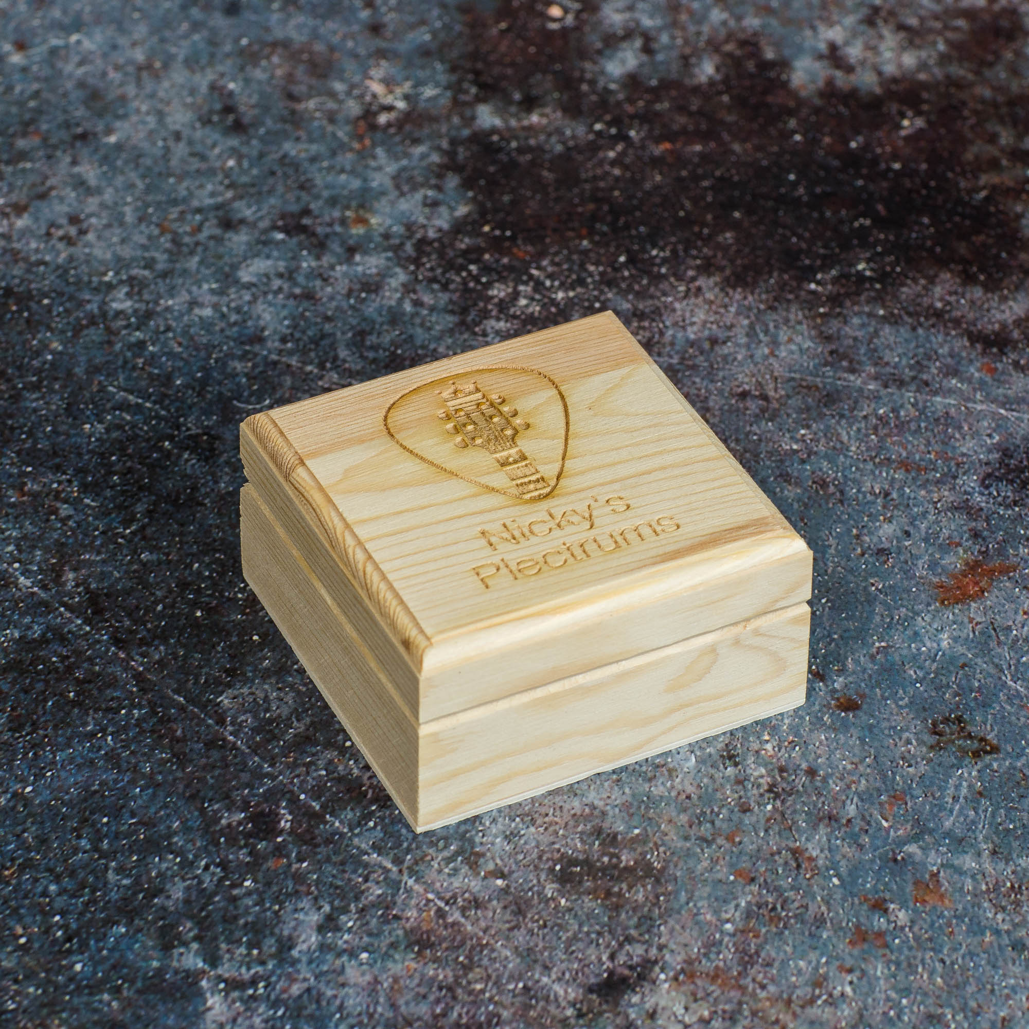 Square wooden box with guitar plectrum imagery and text saying Nicky's Plectrums.