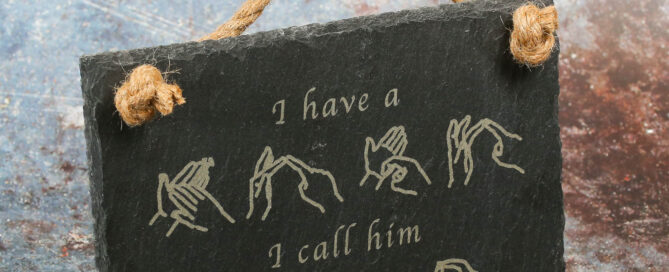 Slate hanging sign using British sign language finger spelling for the words hero and dad. Text says I have a hero I call him dad.