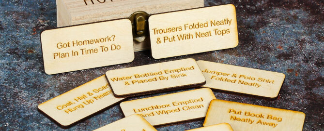 Wooden storage box with Home Time engraved on the lid and wooden tokens with engravings such as put book bag away,water bottled emptied and placed by sink and other home time task examples on them.