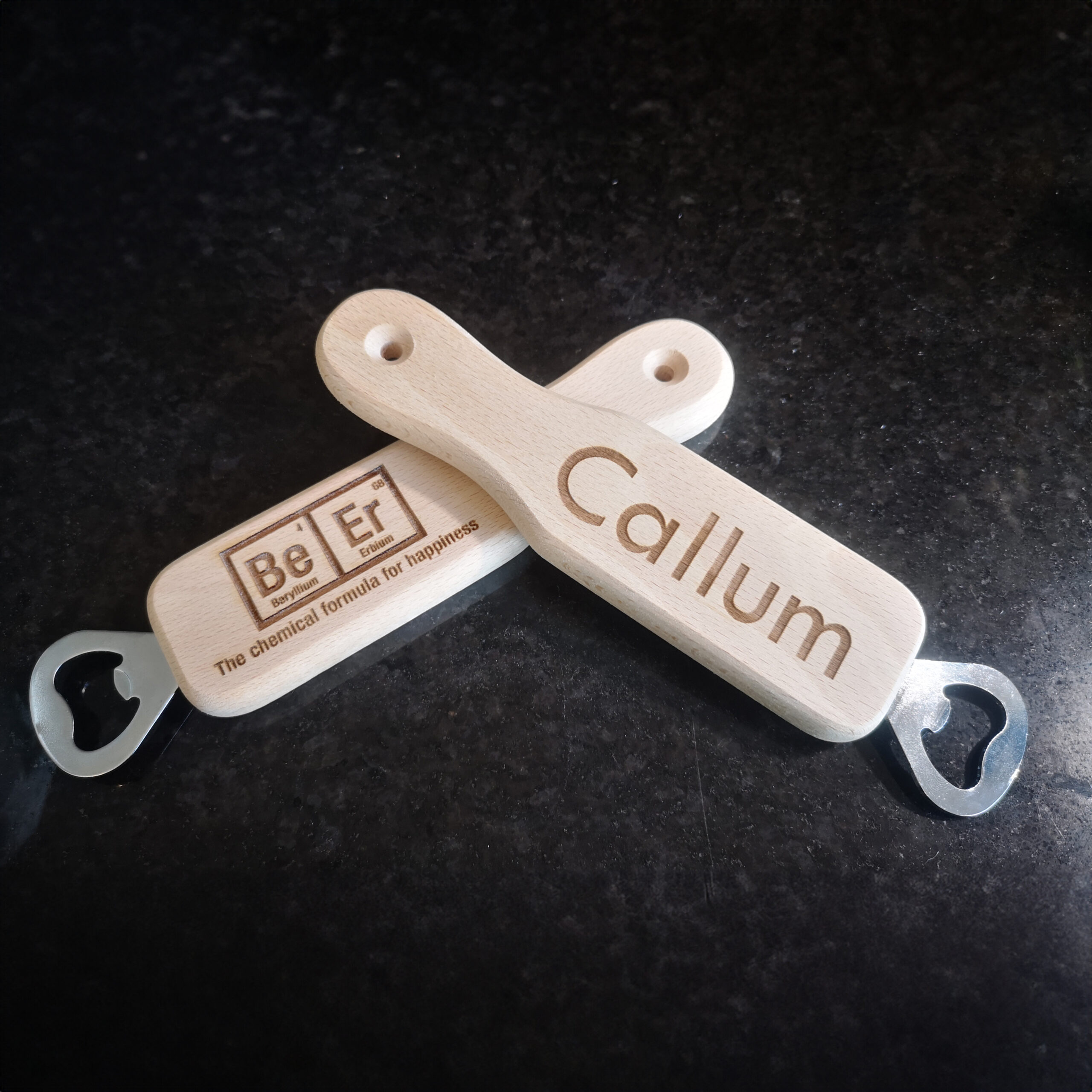 Two bottle openers laying across each other with a name and chemical symbols for beer engraved on them.