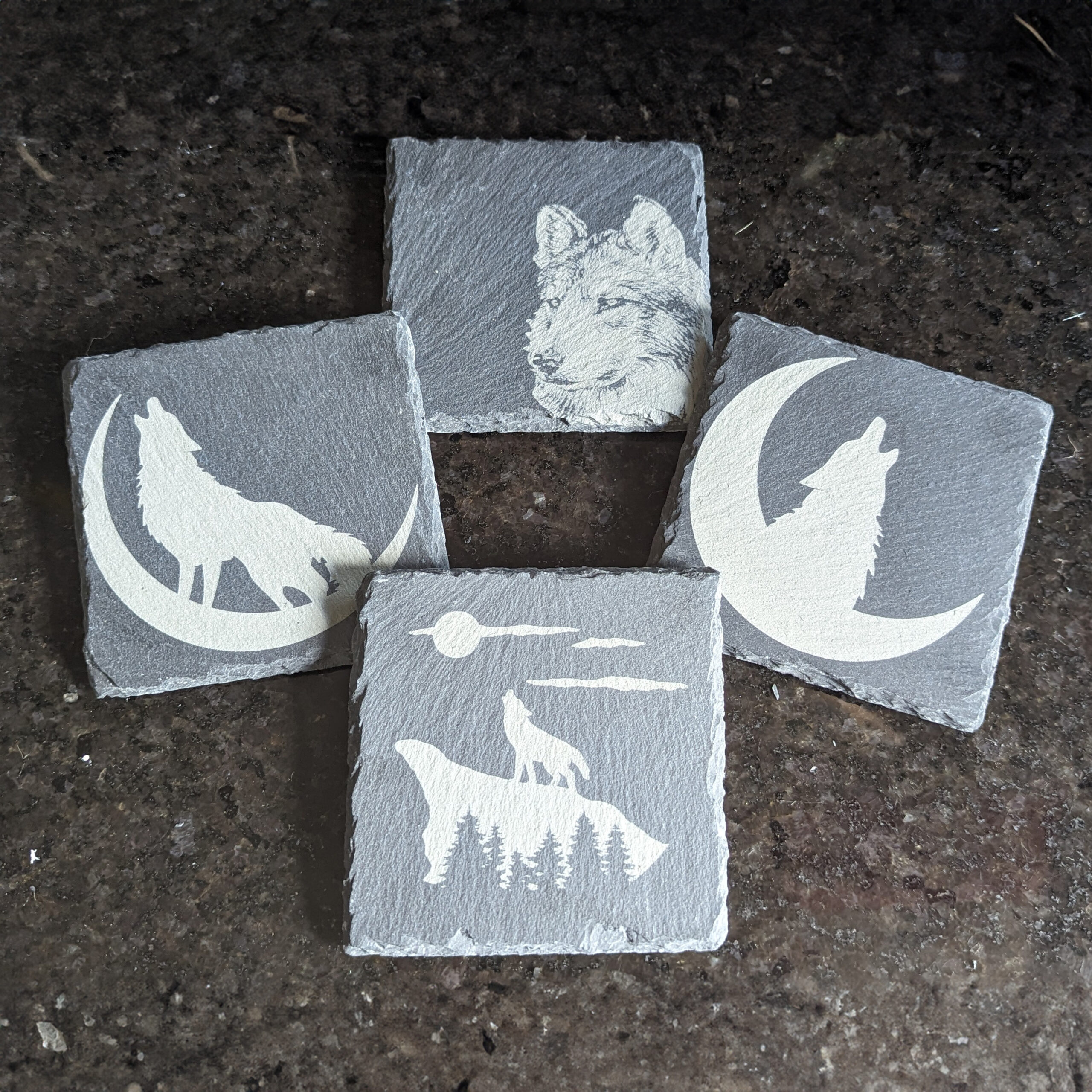 Four slate coasters with imagery of wolves on them. Each one different.