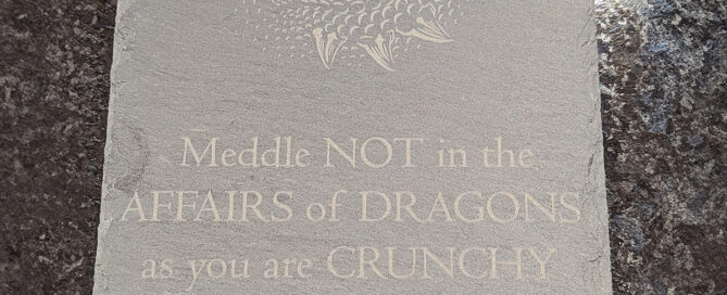 Slate sign with a dragon's eye and text saying Meddle not in the affairs of dragons as you are crunchy and taste good on toast engraved on it.