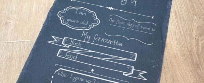 Engraved slate sign with text engraved in segments. Segments include I am (blank) years old, the first day of term is, My favourite book and food is and when I grow up I want to be with space for the answer to be chalk written in.