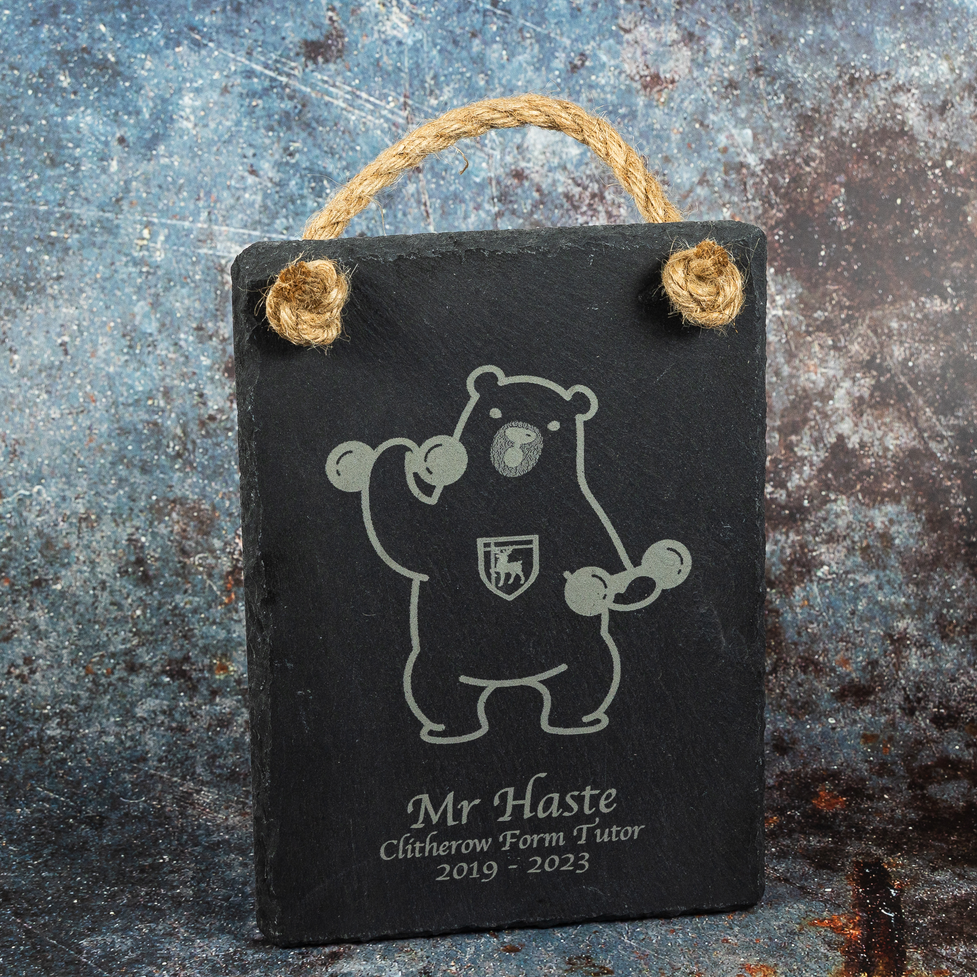 Slate sign engraved with weightlifting polar bear with text underneath saying Mr Haste Clitherow Form Tutor 2019-2023. The sign has hessian rope for hanging.