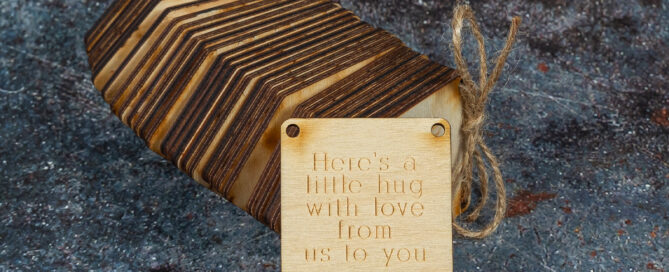 Bundle of wooden bunting flags held together with twine. The foremost flag is laser engraved with "Here's a little hug with love from me to you."
