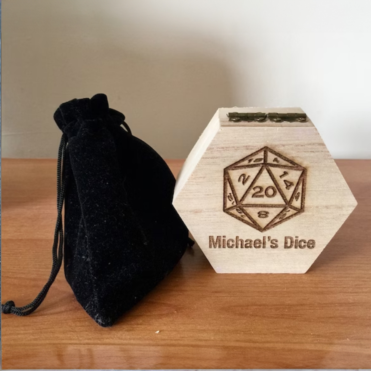Hexagonal wooden box engraved with a 20 sided dice and Michael's Dice. There is a velvet dice pouch by the side of the box.
