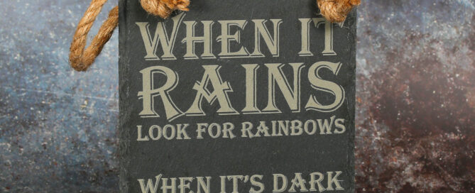 Rectangular slate sign laser engraved with "when it rains look for rainbows. When it's dark look for the rainbows.". There are two holes at the top which are looped with jute rope.