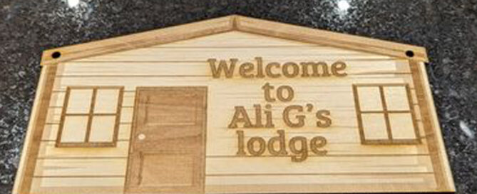 Laser engraved cut out of a wooden lodge style log cabin. Engraved with Welcome To Ali G's Lodge.